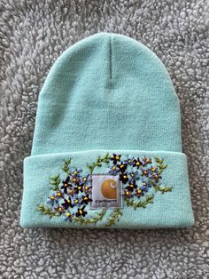 a light blue beanie with flowers on the side and a patch in the middle