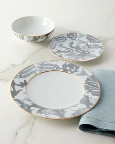 two white and gold plates sitting on top of a table next to a blue napkin