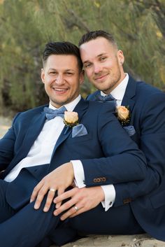 two men sitting next to each other wearing suits and bow ties on their lapels