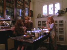 three women sitting at a table in a room with many shelves and glassware on it