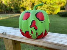 a green pumpkin with red eyes sitting on top of a wooden bench