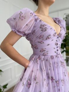 Details: -Lavender tulle with printed flowers -V-neck -Draping -Decorative buttons at the bodice -Cinched waist -Tea-length -A-line silhouette -Side pockets -Short puff sleeves bordered by an elastic band Dream Dress Prom, Teuta Matoshi Dresses, Matoshi Dress, Lavender Floral Dress, Teuta Matoshi, Dress Cottage, Hoco Dresses Long Sleeve, Cottage Core Dress, Dress Fairy