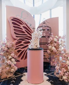 a pink vase sitting on top of a table next to flowers and a birdcage