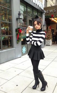 a woman in black and white striped sweater posing on the sidewalk with her cell phone