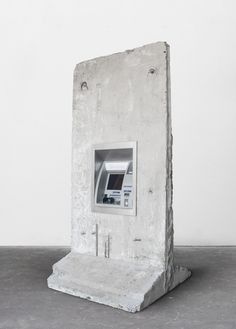 an atm machine sitting on top of a cement block in front of a white wall