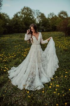 a woman standing in a field wearing a white dress and holding her long sleeves open