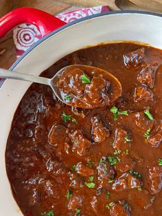 a spoon full of meatballs and sauce in a pot on a table with red napkins