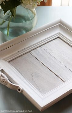 a white wooden tray sitting on top of a table next to a vase with flowers