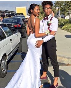 a man and woman standing next to each other in front of parked cars on the street