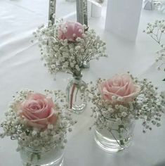 three clear vases with pink roses and baby's breath flowers on a table