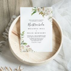 the wedding stationery is on top of a wooden plate with white flowers and greenery