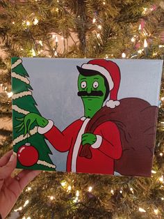 a hand holding up a christmas card with an image of a green man in santa claus's hat