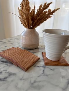 a cup and coaster on a marble table with a plant in the vase next to it