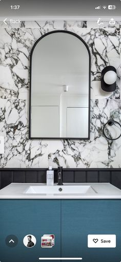 a bathroom with a marble wall and blue cabinet under a large mirror above the sink