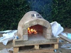 an outdoor pizza oven with flames burning in it's center and several pieces of wood on the ground