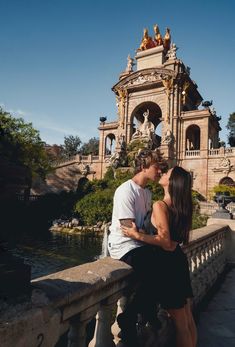 a man and woman are kissing on a bridge near the water in front of an ornate building