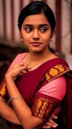 a woman in a red and gold sari with her arms crossed looking at the camera