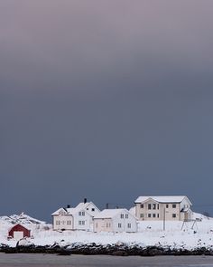 houses on the shore covered in snow under a gray sky with dark clouds above them