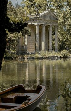 a boat sitting on top of a lake next to a building with columns in the background