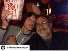 two men pose for the camera while holding up popcorn