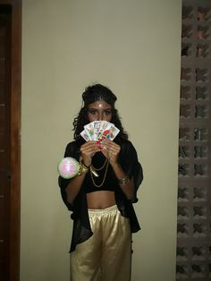 a woman in gold pants and black shirt holding up a deck of cards with both hands