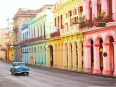 an old car driving down the street in front of colorful buildings