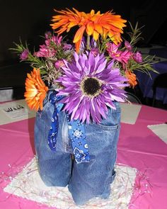 a vase filled with purple and orange flowers on top of a pink cloth covered table