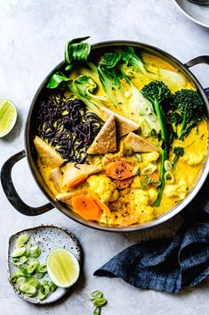 a pot filled with soup and vegetables on top of a table next to sliced limes