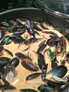 a pan filled with mussels and sauce on top of a stove