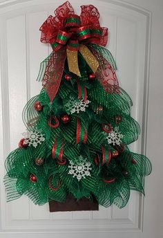 a green christmas tree with red and gold ornaments hanging on the front door for holiday decor