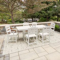 a white table and chairs sitting on top of a stone patio next to a tree