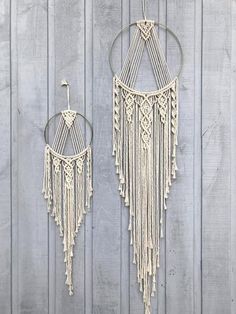 two macrame earrings hanging from hooks on a wooden wall next to each other