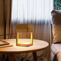 a wooden table with a book on it next to a chair and lamp in front of a window