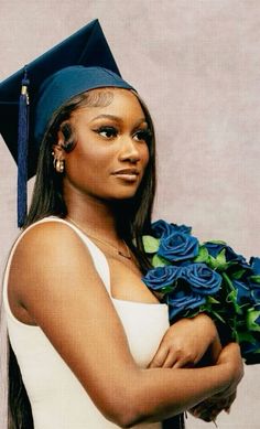 a woman wearing a graduation cap and gown with flowers in her lap, holding a bouquet of blue roses