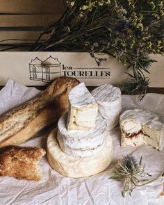 several different types of cheeses and bread on a piece of wax paper next to some flowers