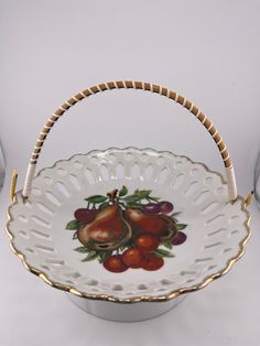 a white and gold basket with fruit painted on the side, sitting on a table