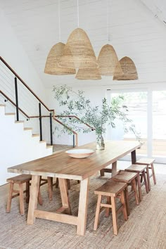 a dining room table with four stools under some hanging lights and plants on the wall