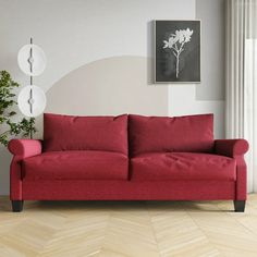 a red couch sitting in front of a white wall next to a potted plant