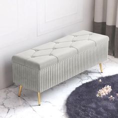 a gray bench sitting on top of a white floor next to a rug and window