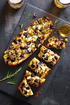 sliced pizza with olives and cheese on a slate platter next to glasses of beer