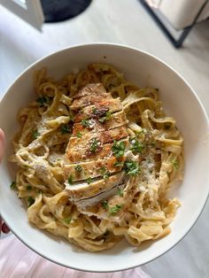 someone holding a bowl of pasta with chicken and parsley