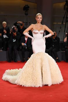 a woman in a long white dress standing on a red carpet with cameras around her