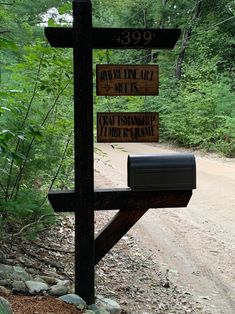 a wooden cross sitting on the side of a dirt road next to a lush green forest