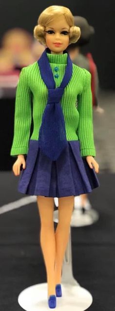 a barbie doll wearing a green sweater and blue skirt with purple shoes on the runway