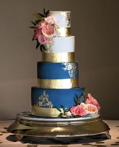 a three tiered cake with blue and gold frosting, pink flowers on top