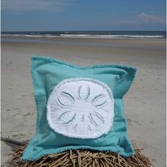 a decorative pillow sitting on top of a pile of straw next to the ocean shore