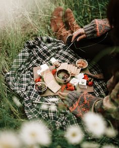 a person sitting in the grass with food on a picnic blanket next to them and flowers