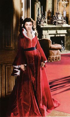 a woman in a red dress standing next to a fireplace