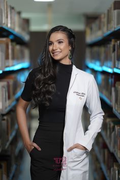 a woman in a white lab coat standing next to bookshelves and smiling at the camera