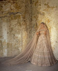 a woman in a wedding dress with a veil on her head standing next to an old wall